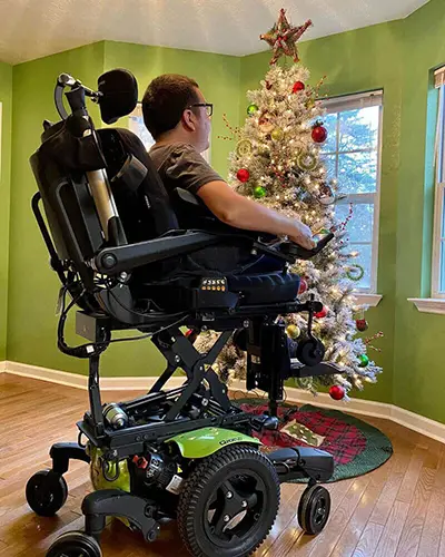 A man using power seat elevate on his wheelchair in front of a Christmas tree