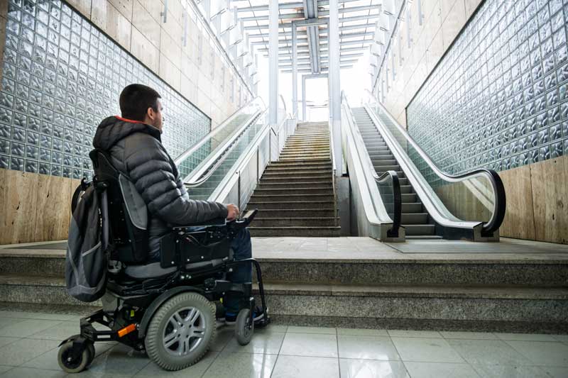 A man using a power wheelchair in front of a set of stairs