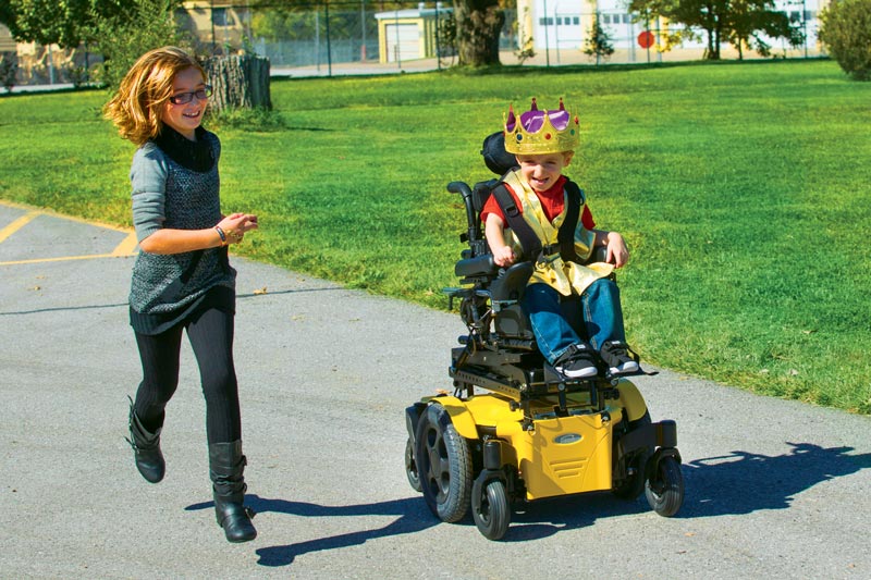 A young boy in a power wheelchair playing with an able-bodied girl