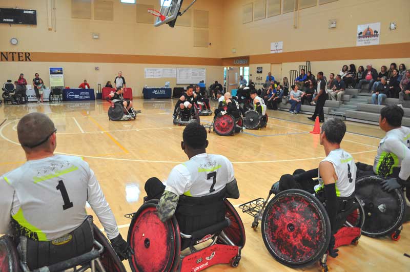 Wheelchair rugby players watch their teammates compete from the sidelines